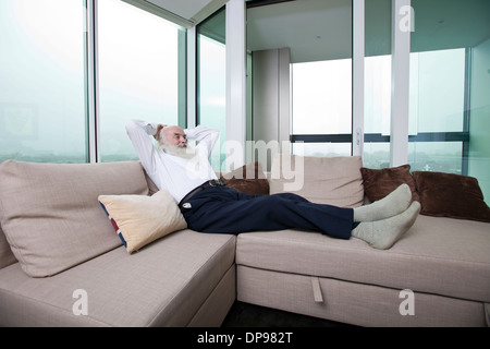 Lunghezza completa di senior uomo rilassante sul divano con le mani dietro la testa a casa Foto Stock