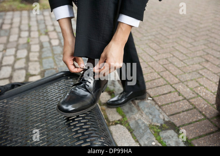 Immagine ritagliata di imprenditore legatura di sua scarpa sul banco di lavoro Foto Stock