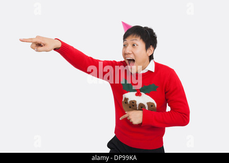Sorpreso uomo che indossa un maglione di Natale mentre sta puntando su sfondo bianco Foto Stock
