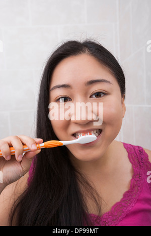 Vista ravvicinata della giovane donna asiatica spazzolare i suoi denti nella stanza da bagno Foto Stock