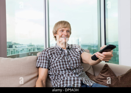 Sorridente metà uomo adulto di guardare la televisione sul divano di casa Foto Stock