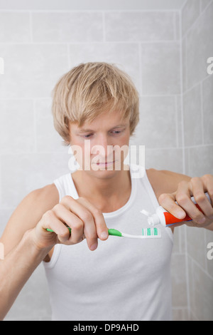 L'uomo la spremitura di dentifricio su uno spazzolino da denti in bagno Foto Stock