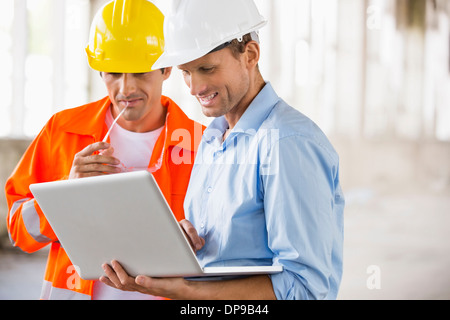 Maschio di architetti che lavorano su laptop al sito in costruzione Foto Stock