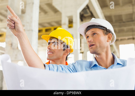 Architetto maschio spiegando piano di costruzione di un collega sul sito in costruzione Foto Stock
