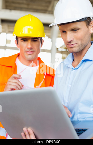 Maschio di architetti che lavorano su laptop al sito in costruzione Foto Stock