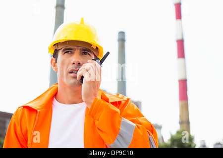 Costruzione maschio Lavoratore che indossa indumenti da lavoro riflettente la comunicazione su un walkie-talkie presso il sito Foto Stock