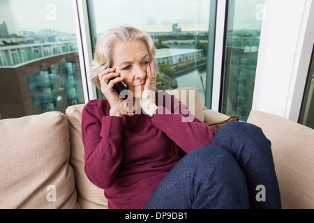 Preoccupato senior donna rispondendo alle smart phone sul divano di casa Foto Stock