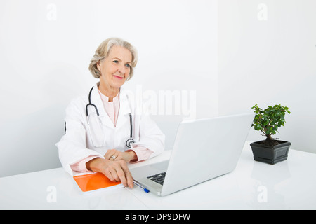 Riflessivo senior medico donna con il computer portatile alla reception in clinica Foto Stock