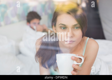 Preciso donna avente il caffè a casa con uomo disteso in background Foto Stock