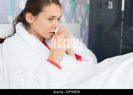 Giovane donna soffrono di freddo utilizzando carta tissue in camera da letto Foto Stock