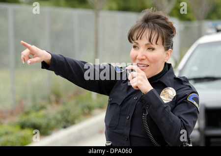 Una femmina di funzionario di polizia i colloqui per la radio con la sua auto di pattuglia in background. Foto Stock