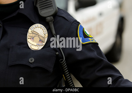 Una vista ravvicinata di un funzionario di polizia è uniforme e stemma con le auto della polizia in background. Foto Stock