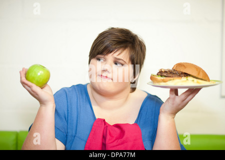 Giovane donna scegliendo tra una mela e un burger Foto Stock