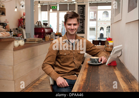 Ritratto di giovane uomo con caffè e tavoletta digitale in cafe Foto Stock