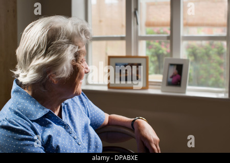 Senior adulto donna seduta in camera guardando fuori della finestra Foto Stock