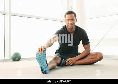 Uomo seduto toccando le dita dei piedi stretching Foto Stock