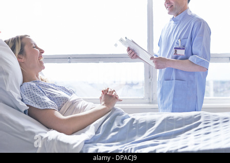 Paziente sdraiato nel letto di ospedale a ridere con un infermiere Foto Stock