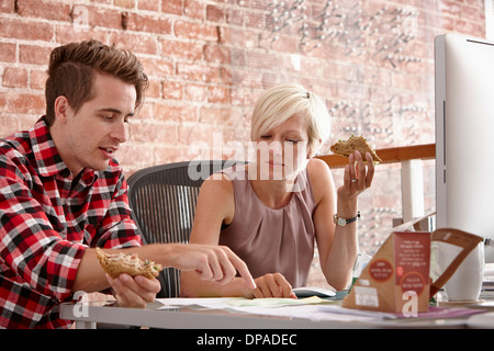 Due colleghi mangiando panini alla scrivania Foto Stock