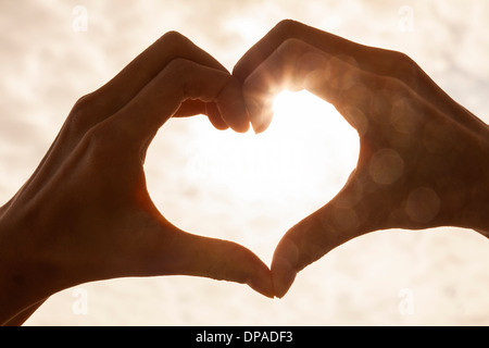 Mano forma di cuore silhouette fatta contro il sole e il cielo di un'alba o al tramonto Foto Stock