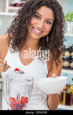 Una bella felice giovane donna o ragazza facendo un fresco frullato di frutta nella sua cucina a casa Foto Stock