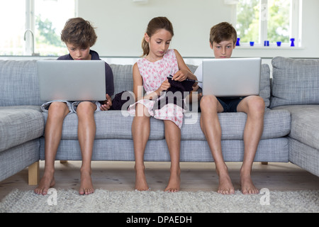 Fratelli e sorelle sul divano con i computer e di lavorazione a maglia Foto Stock