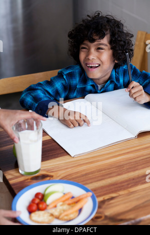 Ragazzo facendo i compiti, persona che serve spuntini e latte Foto Stock