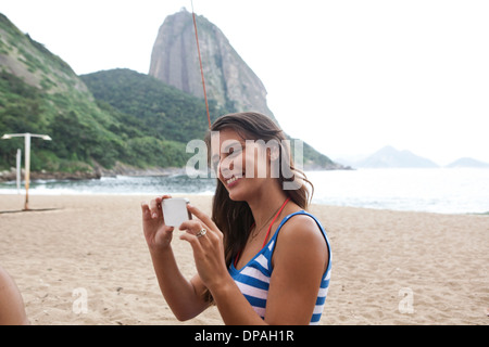 Donna che utilizza fotocamera del telefono sulla spiaggia, Rio de Janeiro, Brasile