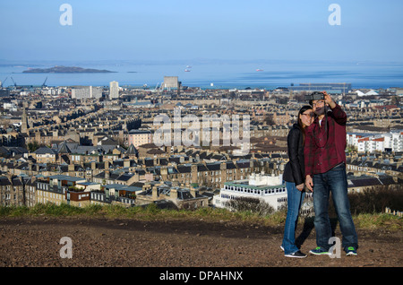 Una giovane coppia asiatica prendere un selfie sulla cima di Calton Hill con il nord di Edimburgo, Leith e il Firth of Forth in background. Foto Stock