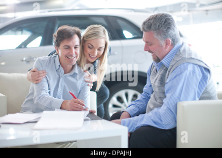 Venditore auto e giovane firma contratto in showroom per auto Foto Stock