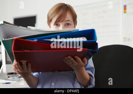 Ragazzo holding pila di raccoglitori ad anelli Foto Stock