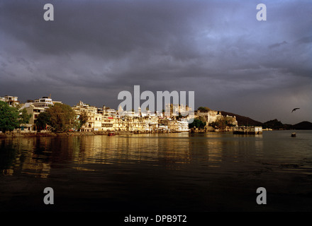 Una vista sul lago Pichola per la balneazione ghats e il palazzo della città in Udaipur nel Rajasthan in India in Asia del Sud. Cielo di tramonto tempestoso vista Meteo Foto Stock