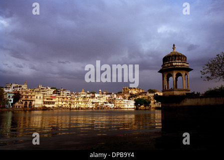 Una vista sul lago Pichola per la balneazione ghats e il palazzo della città in Udaipur nel Rajasthan in India in Asia del Sud. Cielo di tramonto Cielo tempestoso Meteo Foto Stock