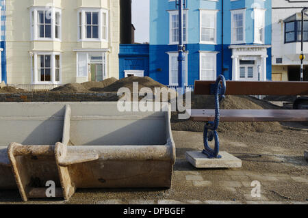 Aberystwyth, Wales, Regno Unito. Il 10 gennaio 2014. Una settimana dopo una violenta tempesta a sovracorrenti e gale force venti danneggiato Aberystwyth sul lungomare, detriti è ancora sparsi intorno alla zona. I lavoratori del consiglio di grado i depositi di alluvione con macchine per separare la sabbia e la pavimentazione in lastre. Lavoro inizia lo smantellamento del grado 2 elencati rifugio pubblico, le cui fondamenta sono stati compromessi dal mare. Credito: keith burdett/Alamy Live News Foto Stock