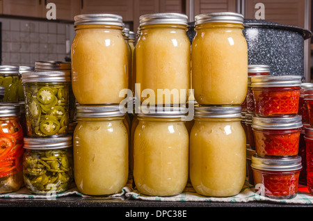 Home conserve di salsa di mele, peperone e pomodoro marmellata impilati sul bancone cucina con acqua calda canner in background Foto Stock