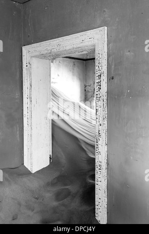 Porta interna in camera riempita con dune di sabbia in casa abbandonata della ex città mineraria oggi una città fantasma in Namibia Foto Stock