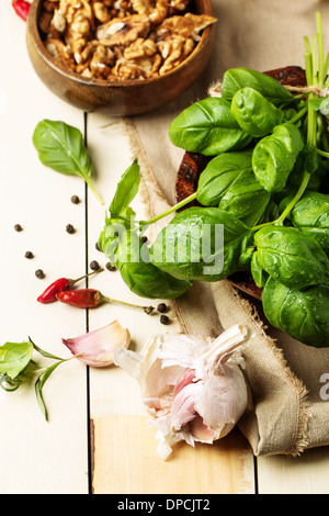 Mazzetto di basilico fresco, tazza di noci, pepe e aglio servita su bianco tavolo in legno. Vedere serie Foto Stock