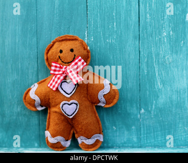 Feltro di Gingerbread Man indossando un rosso Gingham prua, un sorriso e pulsanti di cuori lilla, sorgeva su blu di pannelli di legno Foto Stock