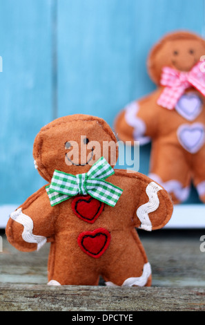 Simpatico giocattolo di feltro shabby chic gingerbread man sul dipinto di blu di tavole di legno, fiaba carattere indossando un sorriso, gingham bow Foto Stock