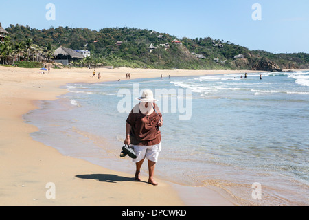 A piedi nudi vecchia donna che porta scarpe e indossando cappello di paglia guarda per i serbatoi a bordo di mare San Agustinillo beach il giorno di Natale 2013 Foto Stock