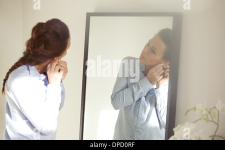 Bellissima femmina mettendo sul suo orecchini di fronte a specchio. Imprenditrice di vestirsi per lavoro. Caucasian modello femminile Foto Stock