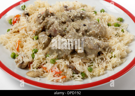 Cremosa di agnello korma curry guarnito con semi di sesamo tostati e servite su un letto di verdure, Pilaf close-up Foto Stock