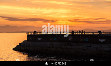 La gente fuori per una passeggiata serale godere di un bellissimo tramonto su un frangiflutti in Victoria British Columbia, Canada Foto Stock