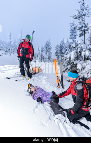 Pattuglia di sci ad aiutare la donna con la gamba rotta giacente nella neve Foto Stock