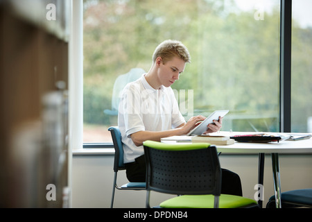 Ragazzo adolescente utilizzando digitale compressa nella libreria Foto Stock