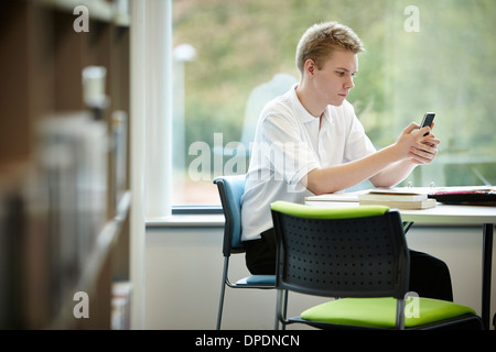 Ragazzo adolescente utilizzando il cellulare in biblioteca Foto Stock