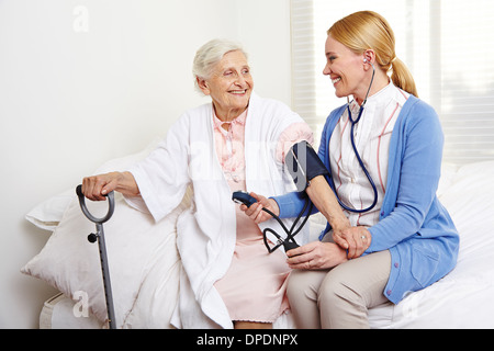 Infermiera geriatrica la misura della pressione del sangue di senior citizen donna nella casa di cura Foto Stock