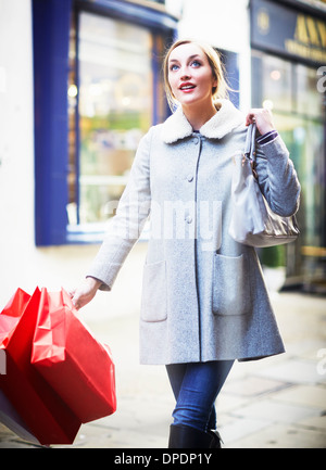 Giovane donna camminare per strada portando shopping bag Foto Stock
