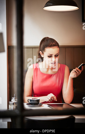 Giovane donna seduta al cafe con bevanda calda, digital tablet e smartphone Foto Stock