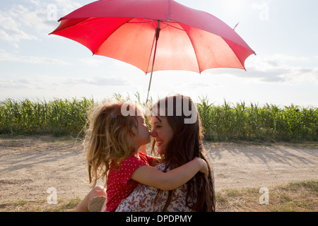 Madre e figlia abbracciando sotto ombrellone rosso Foto Stock