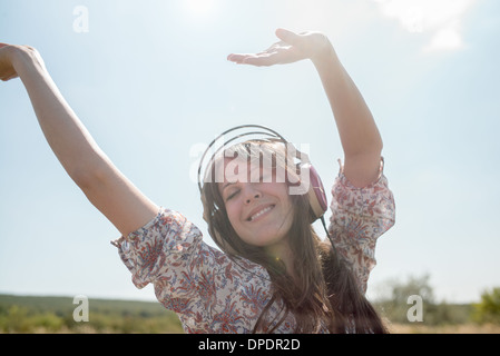 Ritratto di metà donna adulta dancing in campo indossando le cuffie con le braccia sollevate Foto Stock